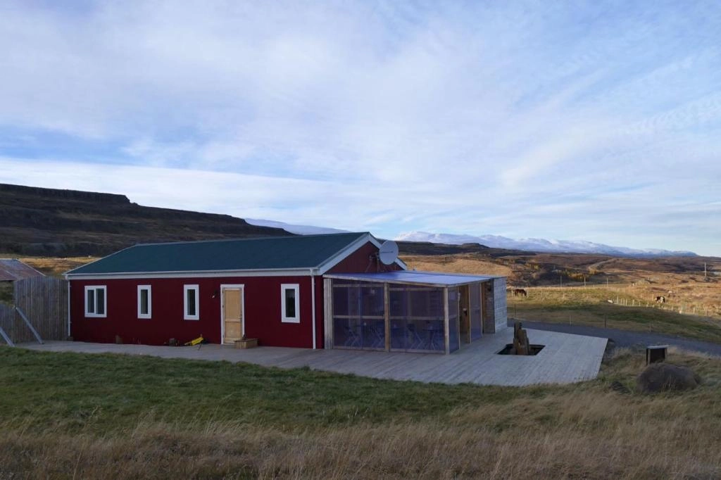 Red Litlabjarg guesthouse with green roof and large glass-walled terrace in the Icelandic countryside